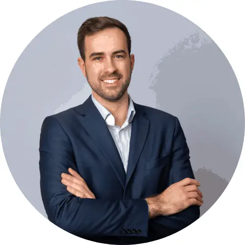 Mitch Miller, ENA. Mann i en mørkeblå dress står med armene i kors og smiler inn i et kamera. Han står med en grå bakgrunn.