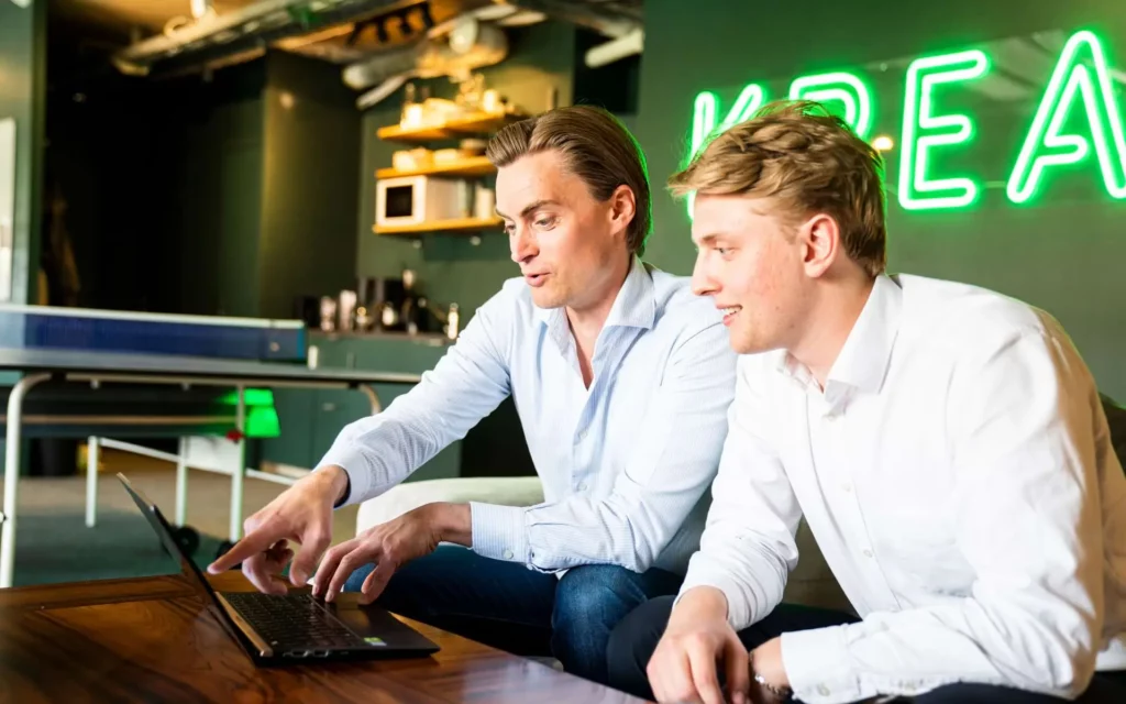 To menn diskuterer på Kreas kontor foran en bærbar datamaskin og med et bordtennisbord i bakgrunnen.